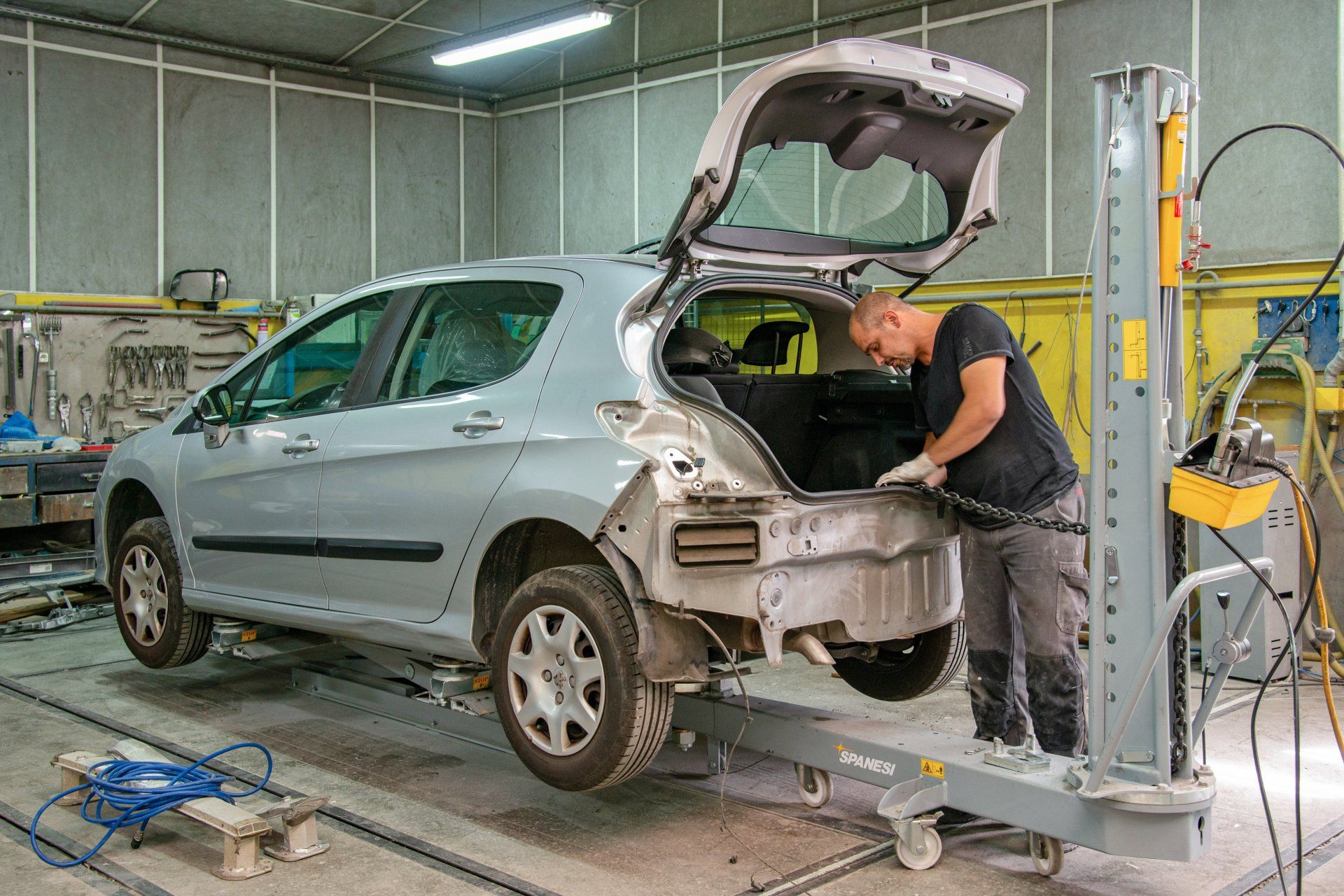 Technicien qui intervient à l'arrière d'une auto citadine surélevée pour sa carrosserie.