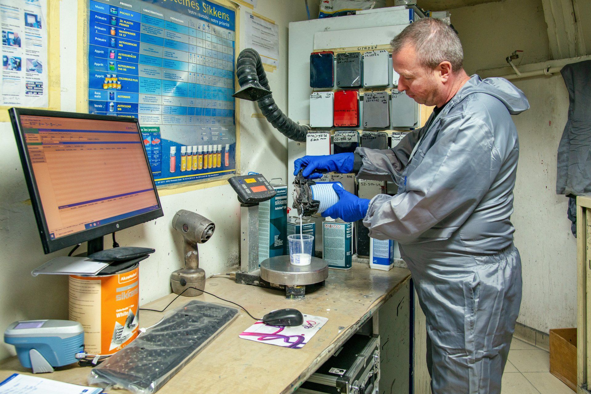 Technicien en combinaison grise en train de doser un produit liquide pour carrosserie.