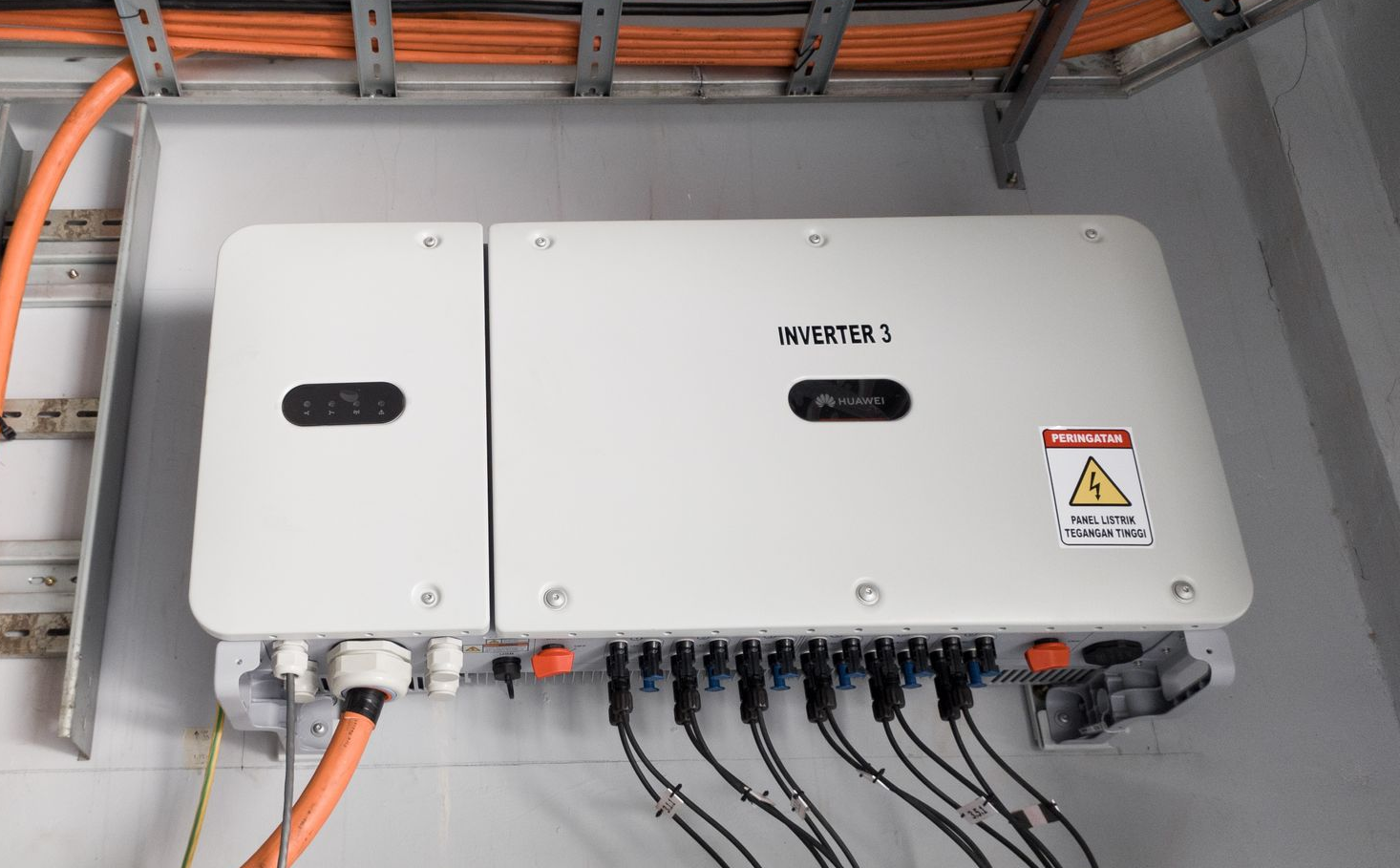 Onduleur solaire blanc fixé au mur avec des câbles orange et noirs, et une étiquette d'avertissement.