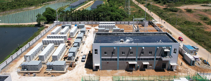 Vue aérienne d'une installation industrielle comprenant plusieurs bâtiments et conteneurs, entourée d'une clôture et d'une route.