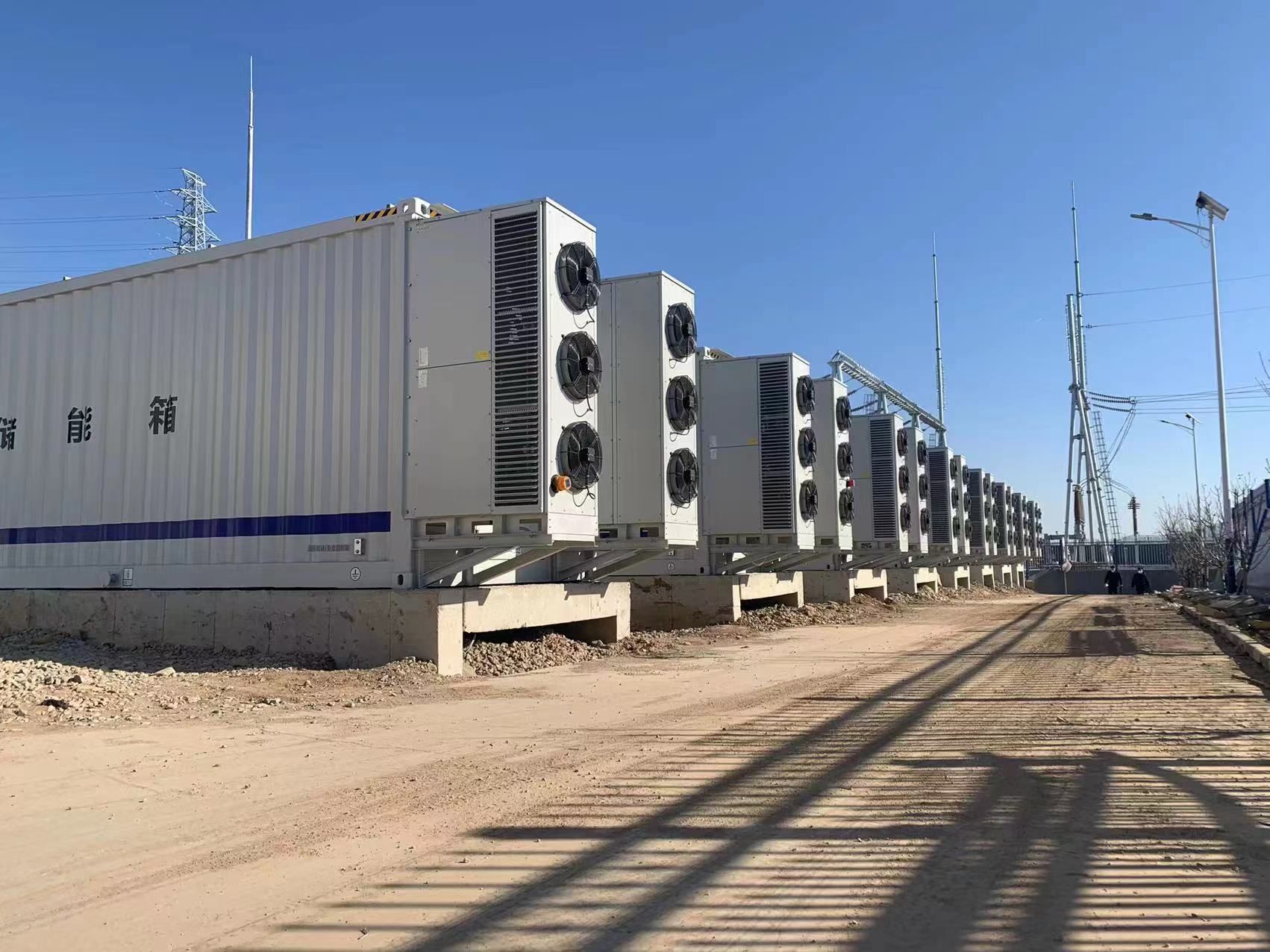 Des rangées de conteneurs maritimes blancs équipés de grands ventilateurs de refroidissement, probablement un centre de données, sous un ciel d'un bleu éclatant.