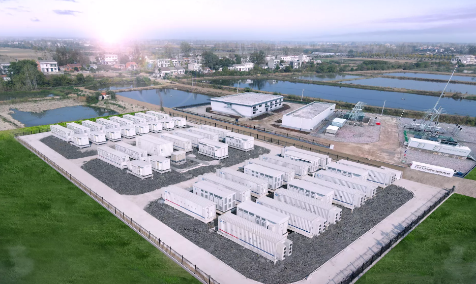 Système de stockage d'énergie par batteries, rangées de conteneurs blancs, sur fond de bâtiments et de points d'eau.