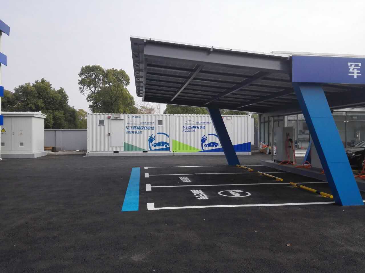 Station de recharge pour véhicules électriques avec auvent bleu et blanc, emplacements de recharge marqués sur l'asphalte.