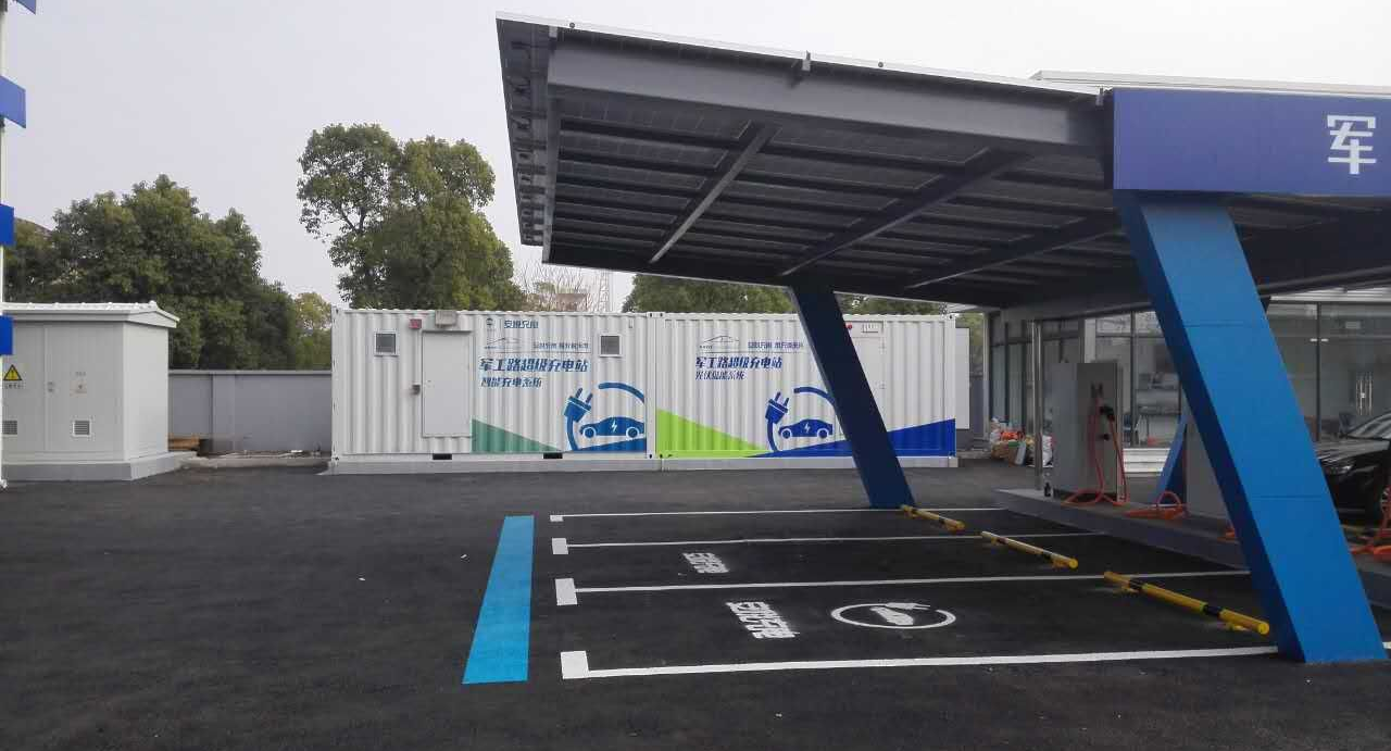 Station de recharge pour véhicules électriques avec marquages ​​bleus et blancs, auvent et conteneur.