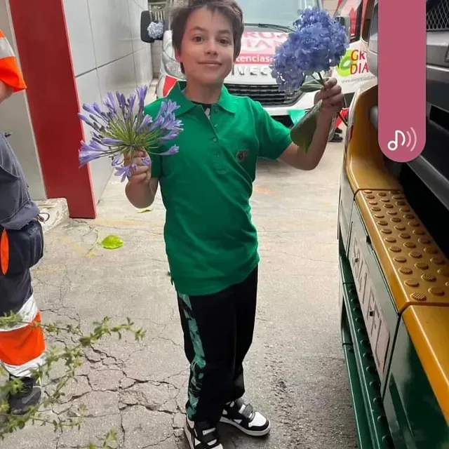 Un niño con una camisa verde sostiene un ramo de flores moradas.