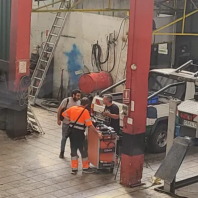 Un grupo de hombres están de pie en un garaje hablando entre ellos.