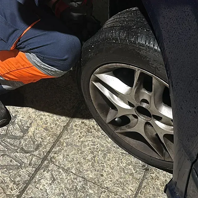 Una persona está arrodillada junto a una rueda de coche.