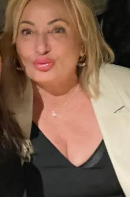 Una mujer con un top negro y una chaqueta blanca posa para una fotografía.