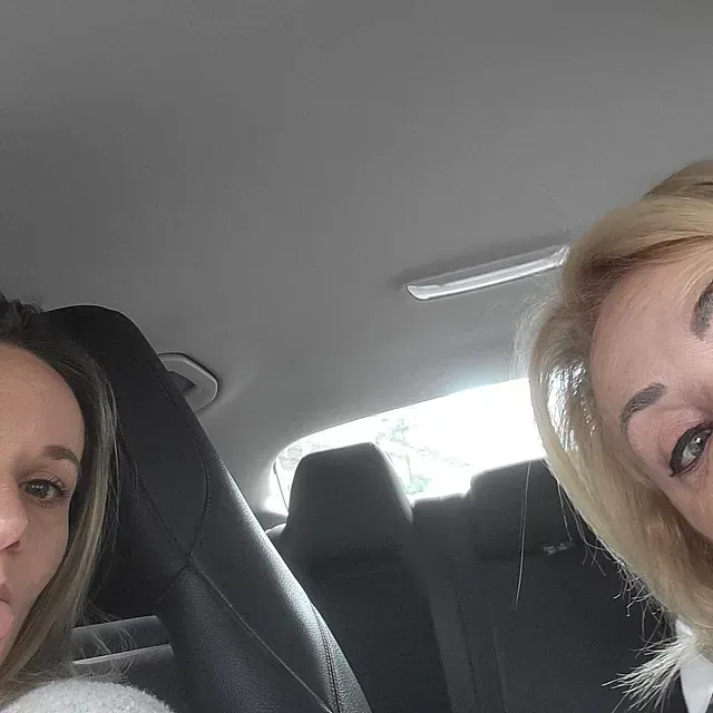 Dos mujeres posan para una fotografía en el asiento trasero de un coche.