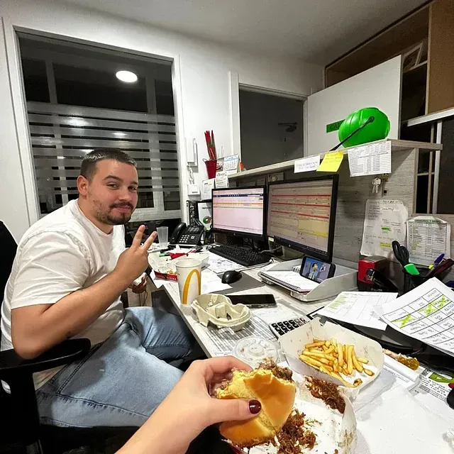 Un hombre está sentado en un escritorio comiendo una hamburguesa y papas fritas.
