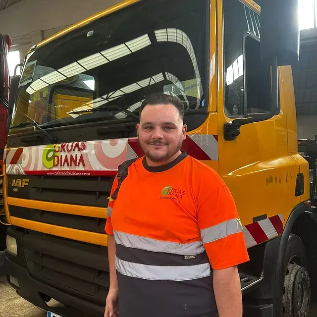 Un hombre con una camisa naranja está parado frente a un camión que dice 