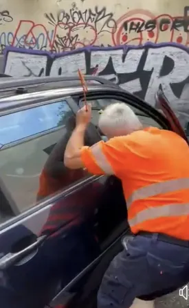 Un hombre con una camisa naranja intenta abrir la puerta de un coche.