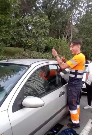 Un hombre con un uniforme naranja y blanco está de pie junto a un coche.