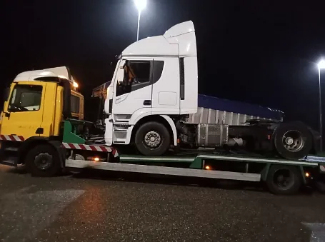 Un camión blanco está siendo remolcado por un camión amarillo.