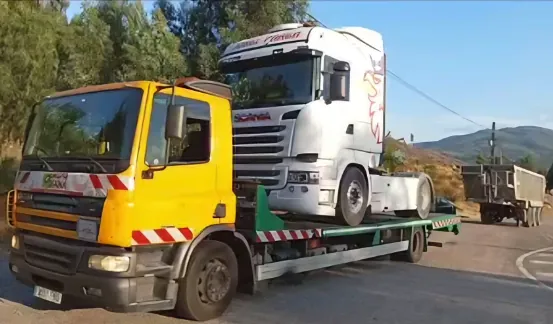 Una grúa amarilla transporta un camión semirremolque blanco sobre un remolque de plataforma.