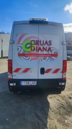 Una camioneta blanca con la palabra Gruas Diana en la parte trasera está estacionada en un lote de tierra.