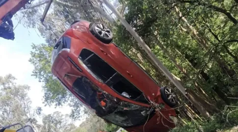 Un coche rojo está colgado boca abajo de una grúa en el bosque.