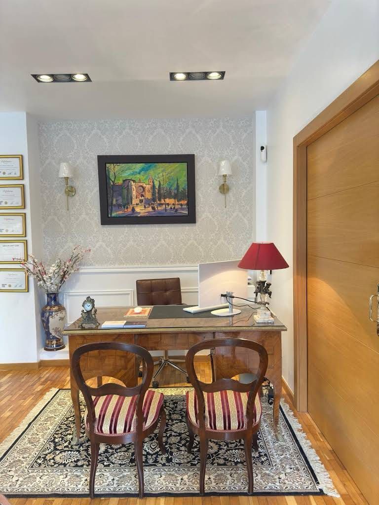 Una habitación con un escritorio, sillas, una lámpara y un cuadro en la pared.