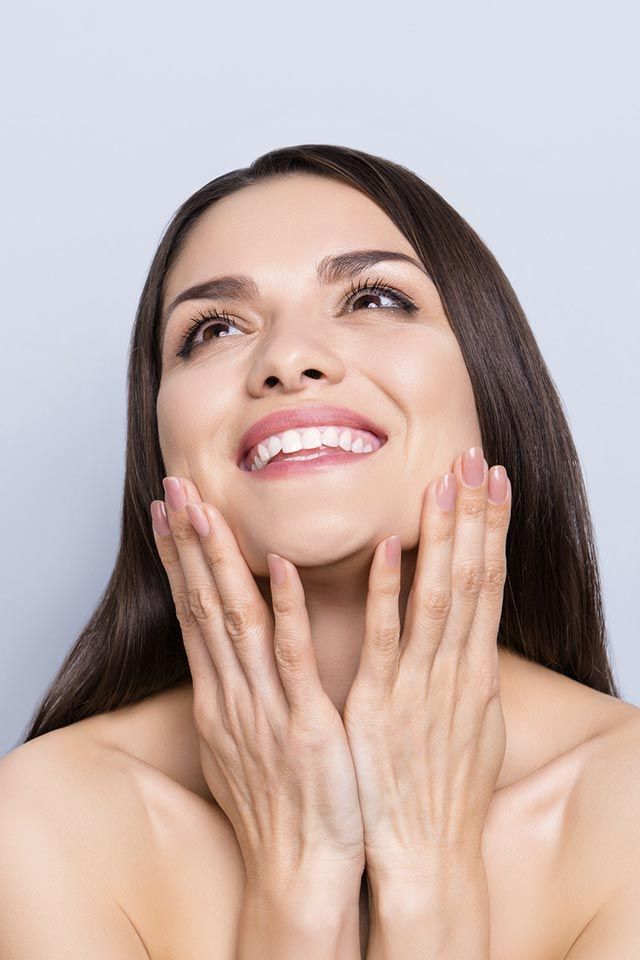 Una mujer sonríe y se toca la cara con las manos.