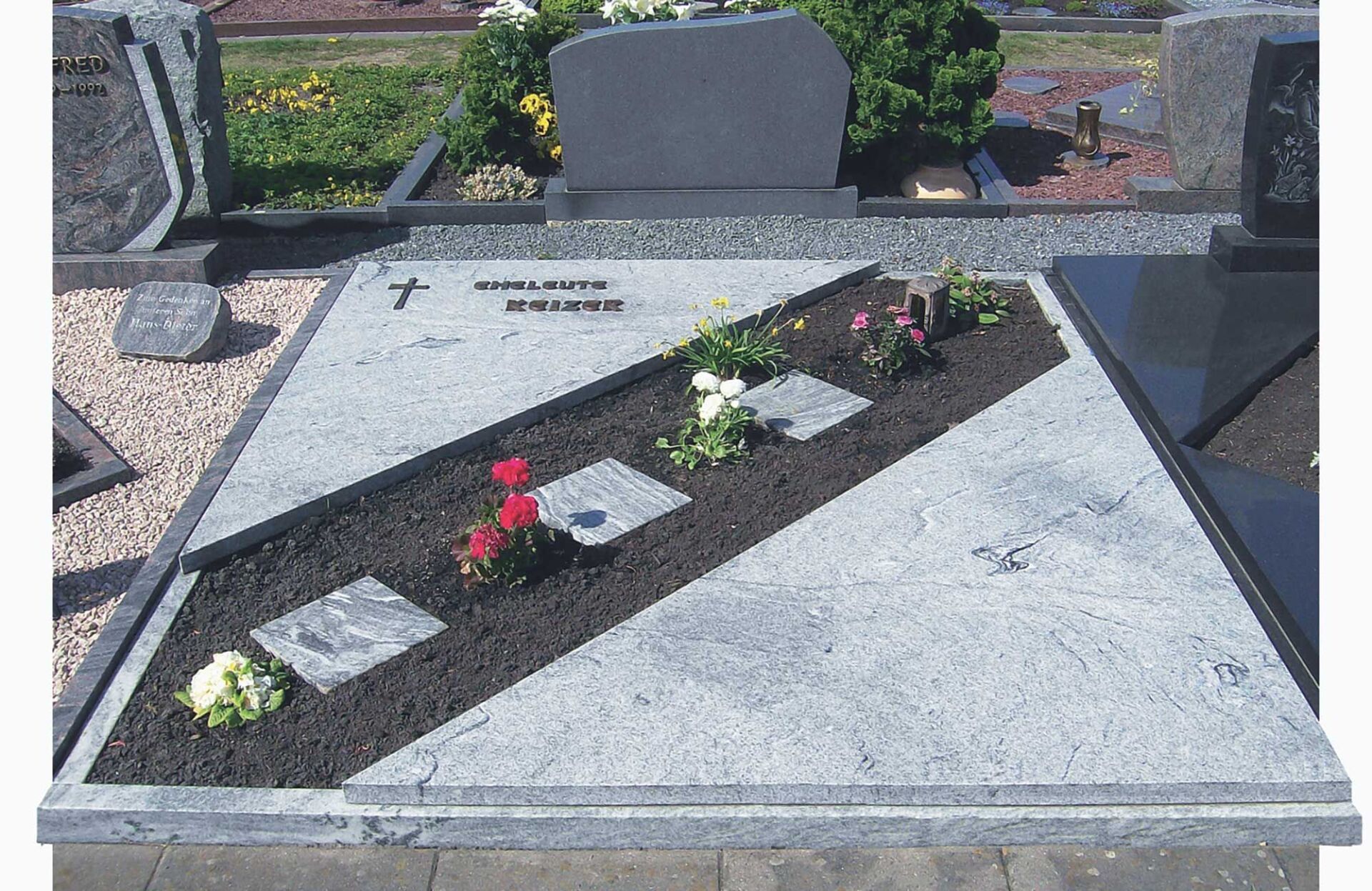 Grab, überwiegend mit Steinplatte bedeckt und Blumenschmuck