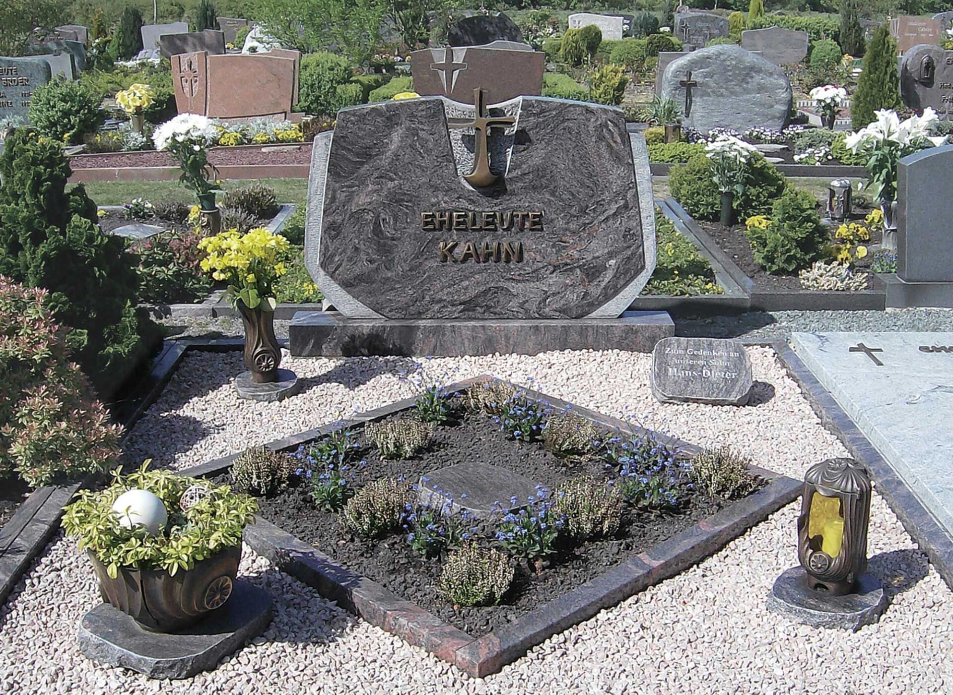 kunstvoll dekoriertes Grab mit beschriftetem Grabstein, Steinplattenelement, Kies und Pflanzen