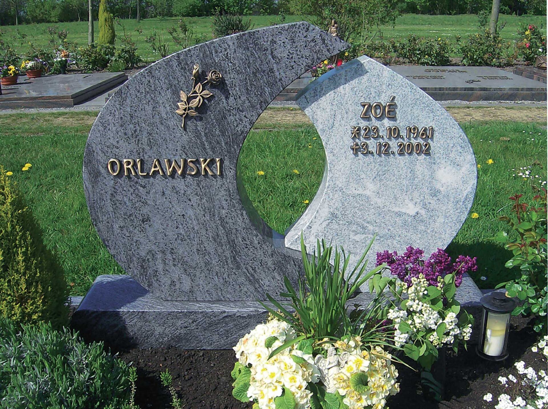 kunstvoll dekoriertes Grab mit beschriftetem Grabstein, Steinplattenelement, Kies und Pflanzen