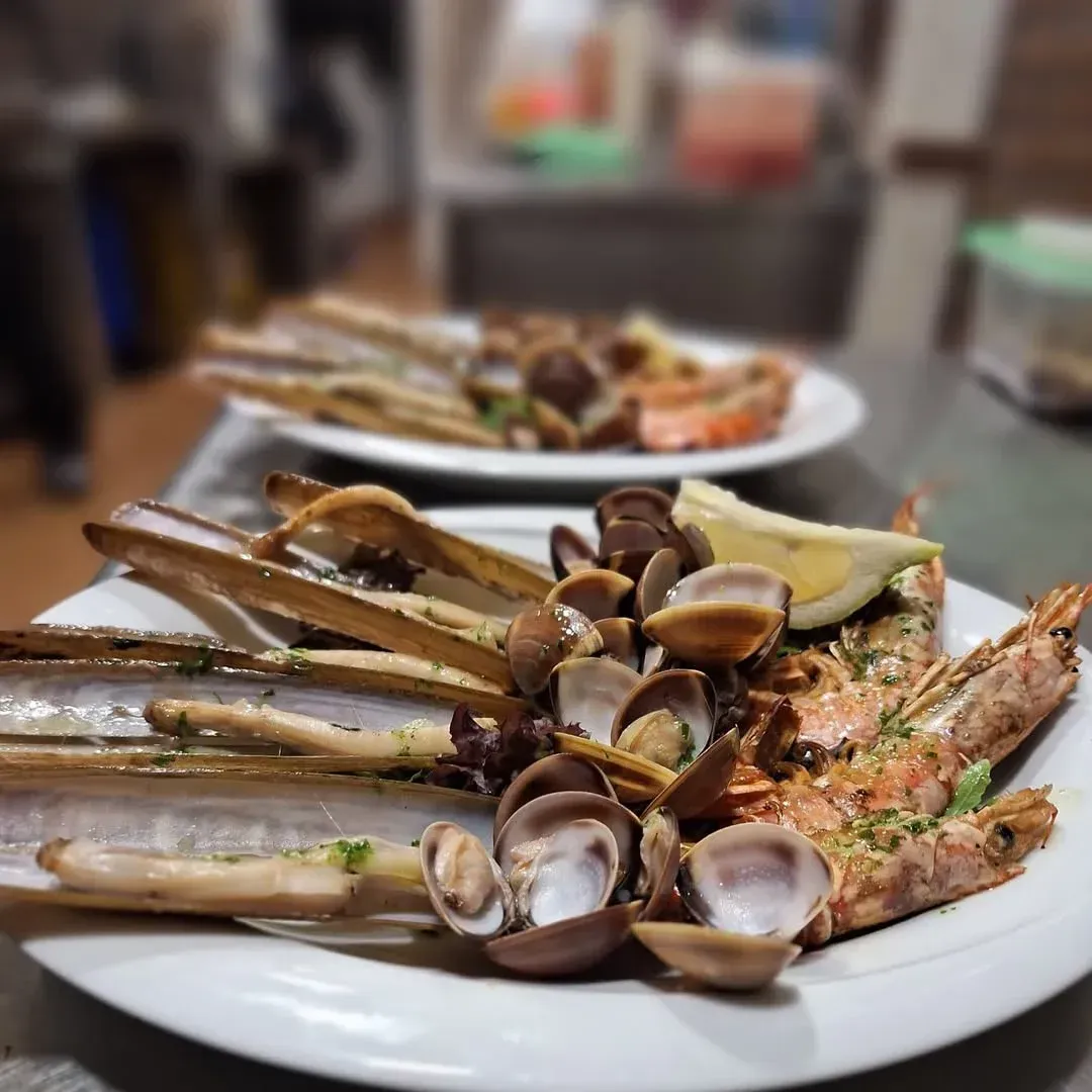 Platos de mariscos: navajas, almejas y camarones a la plancha, adornados con limón.