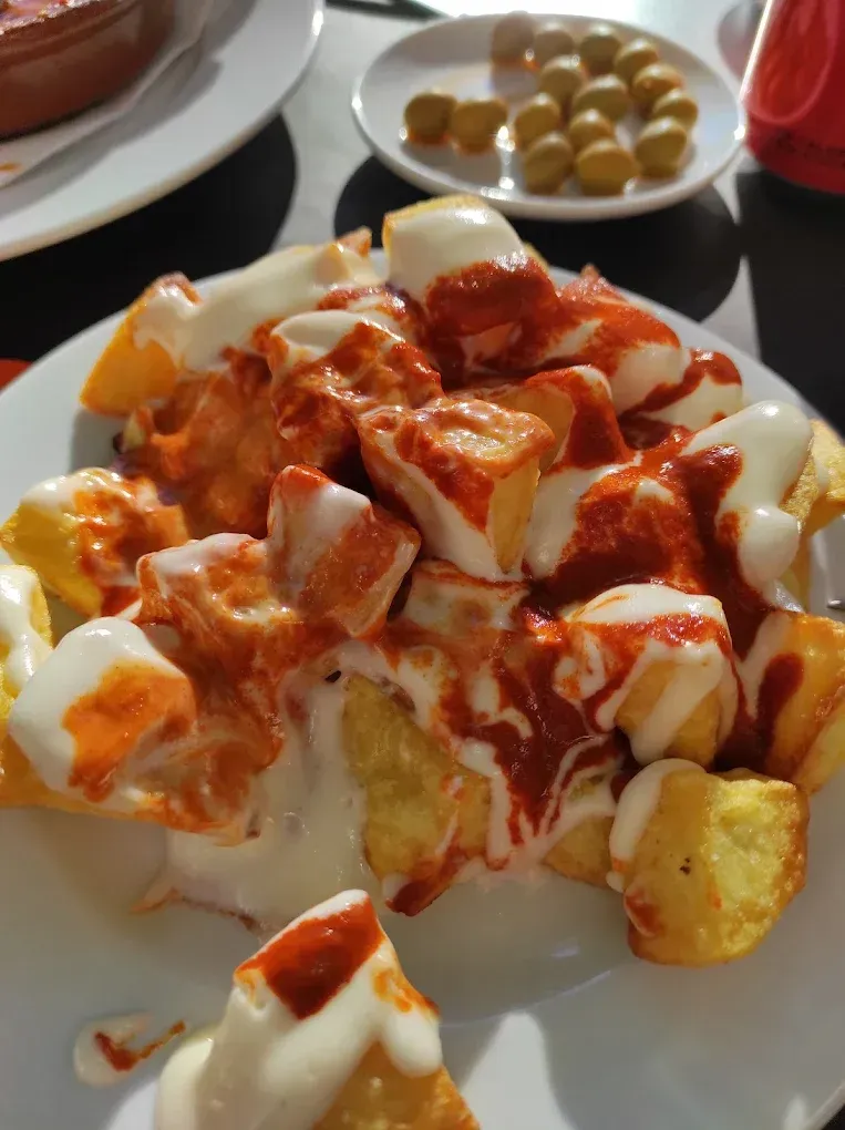 Patatas bravas: dados de patata fritos con salsa roja y alioli blanco, servidos en un plato blanco.