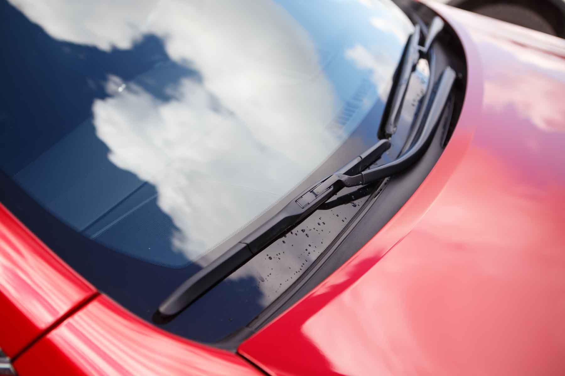 Vue sur pare-brise d'une voiture rouge avec le reflet des nuages