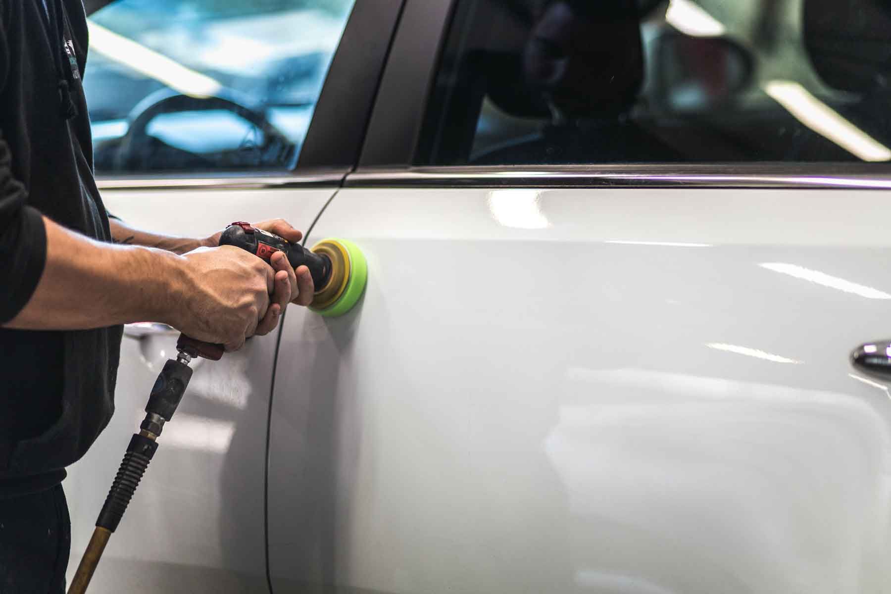 Technicien spécialisé dans la carrosserie polissant une porte arrière de voiture