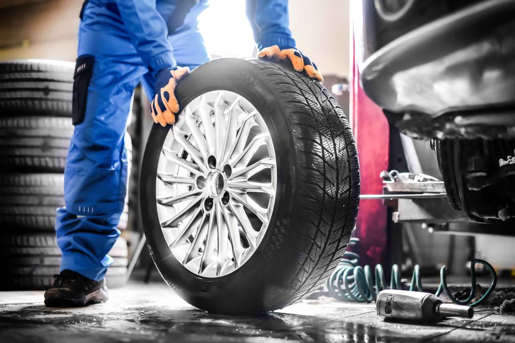 Mécanicien faisant rouler une roue de voiture dans un garage automobile