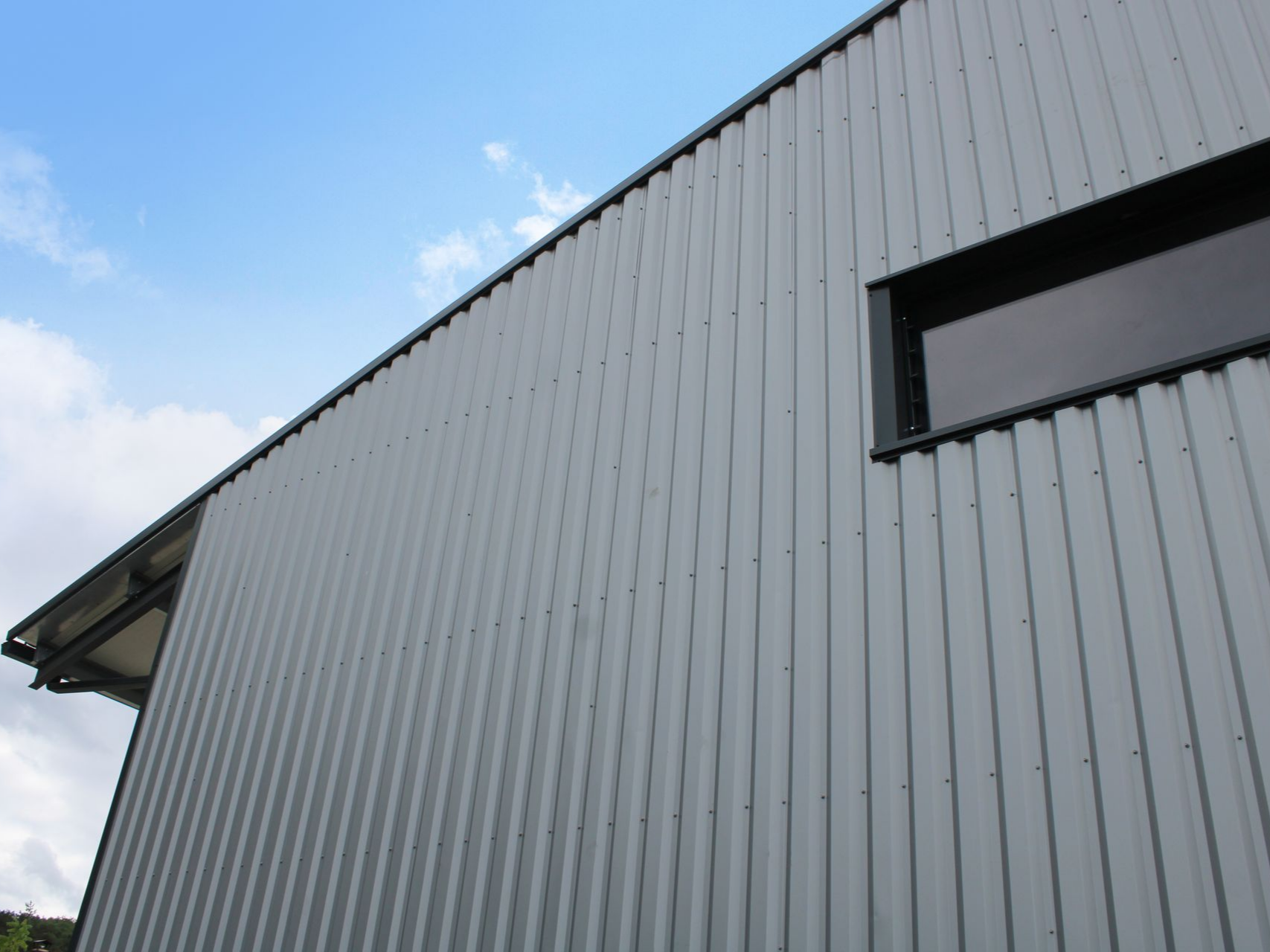Bâtiment en tôle ondulée grise avec une petite fenêtre sombre.