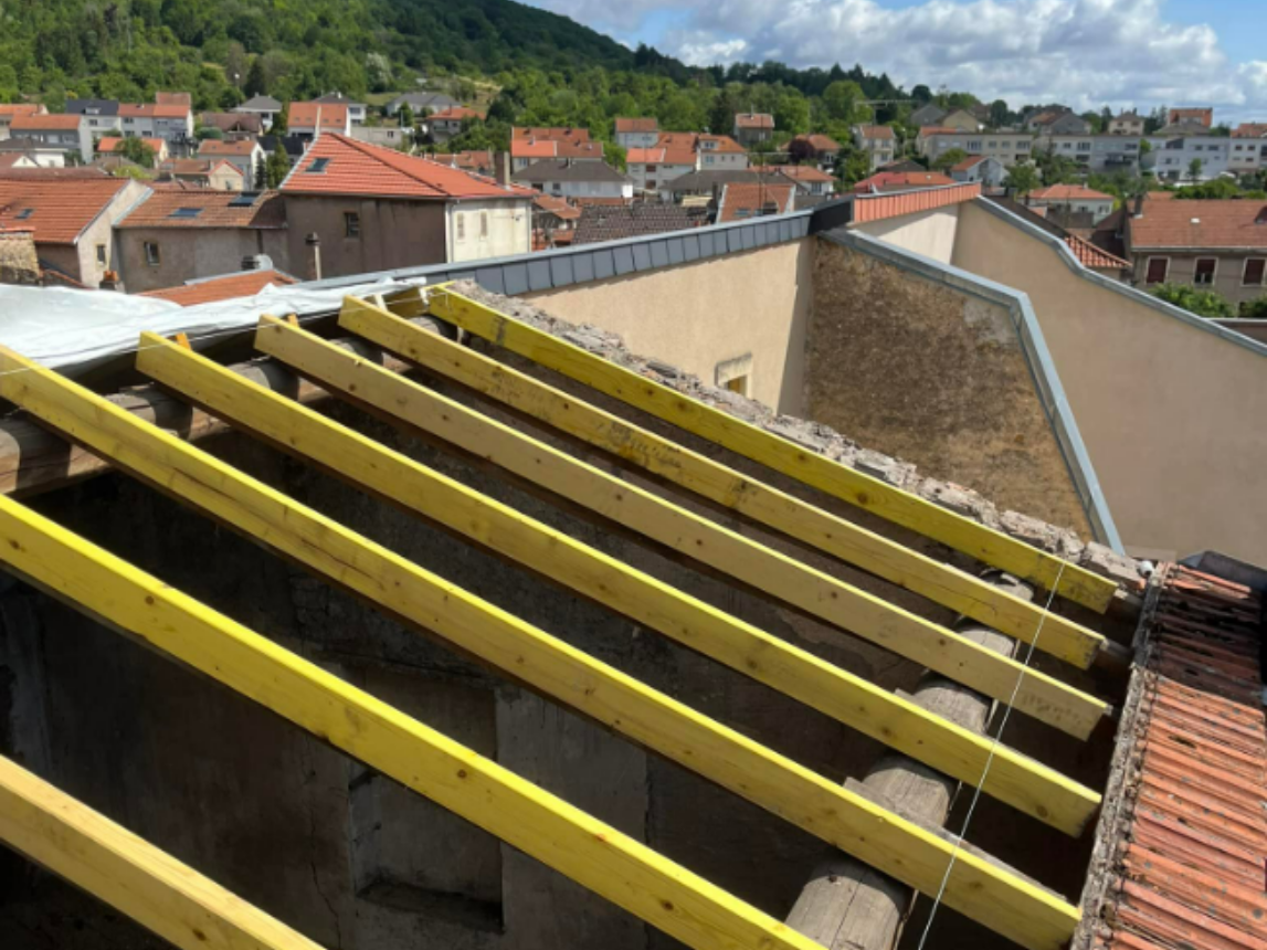 Poutres de toit en bois posées sur une structure en briques. Tuiles rouges et façade du bâtiment visibles.
