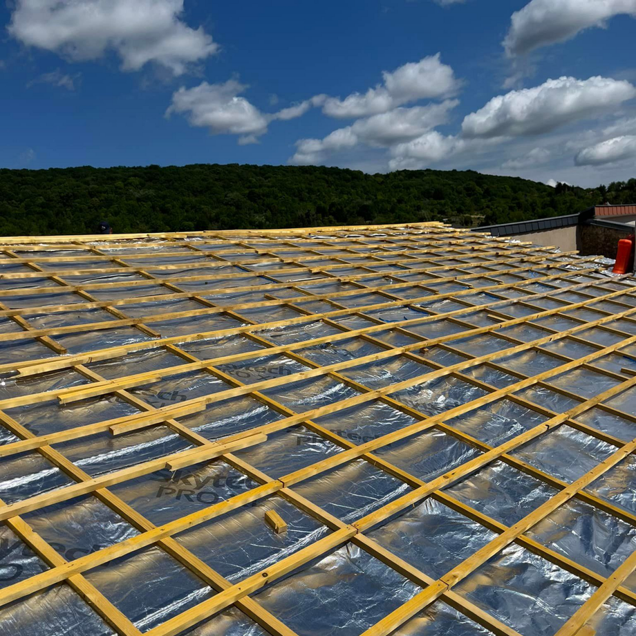 Toiture en construction avec ossature en bois, isolation et ciel bleu.