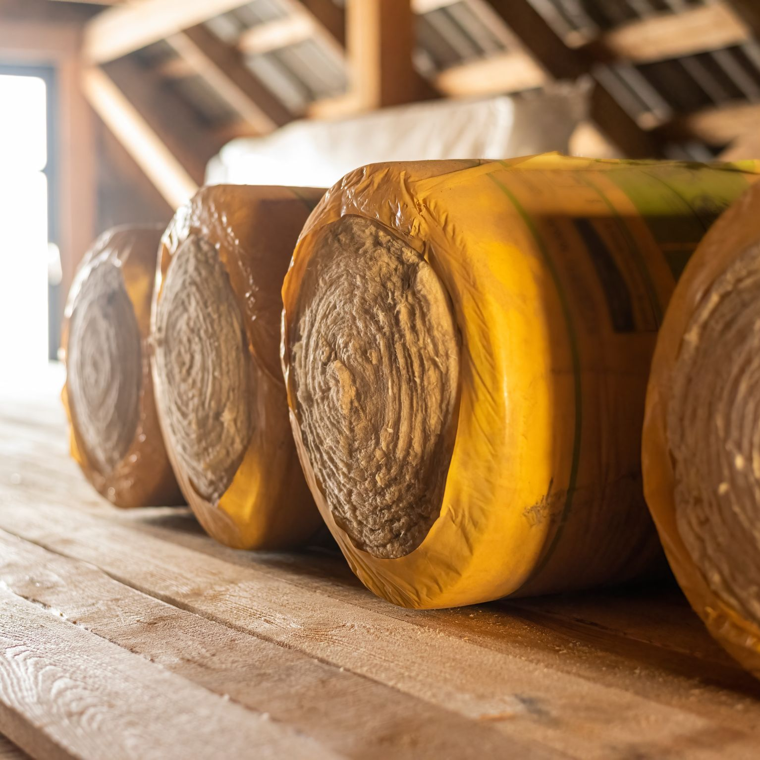 Rouleaux d'isolant enveloppés dans du plastique jaune, empilés sur des planches.
