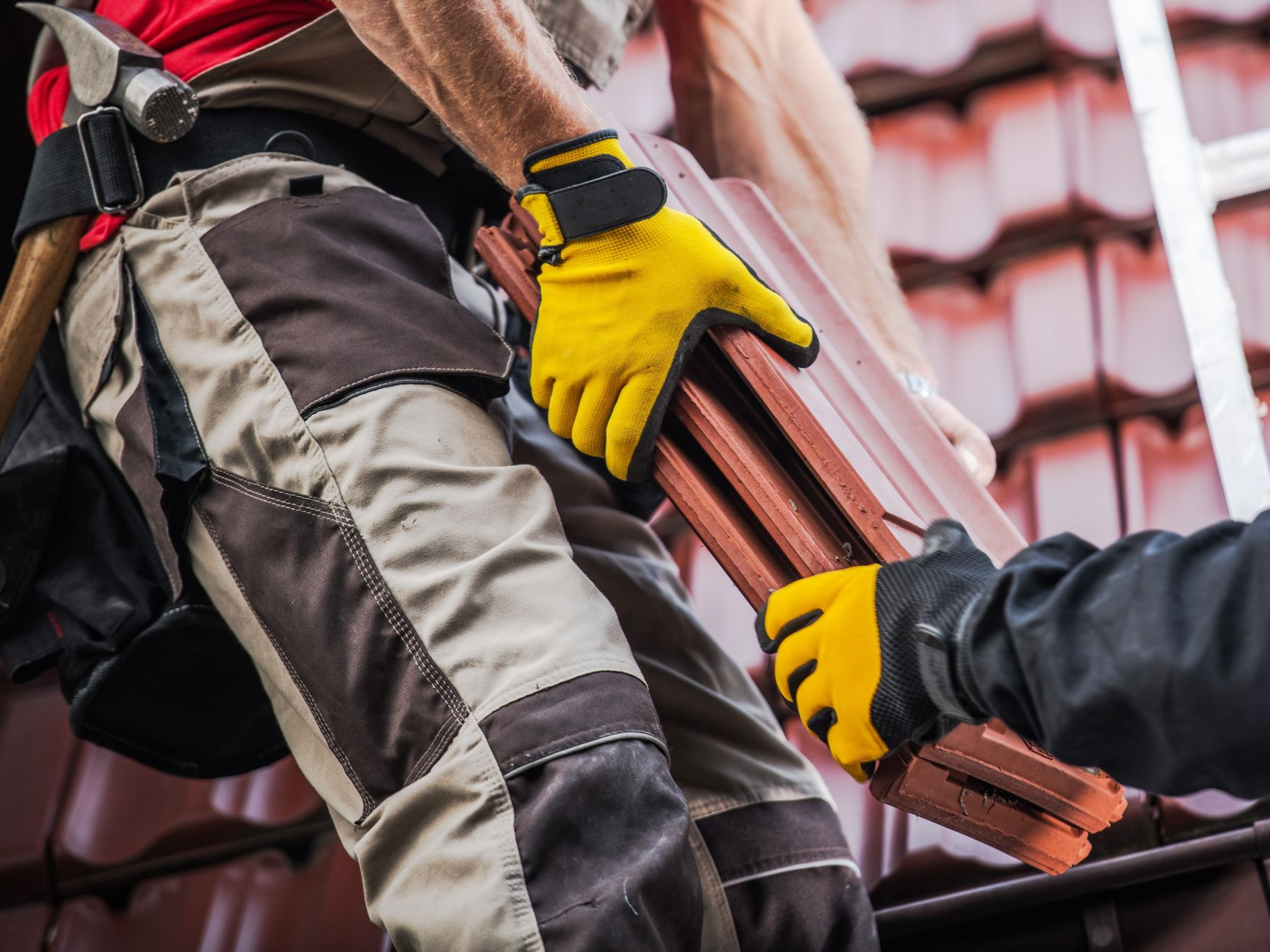 Deux couvreurs en équipement de sécurité manipulant des tuiles rouges.