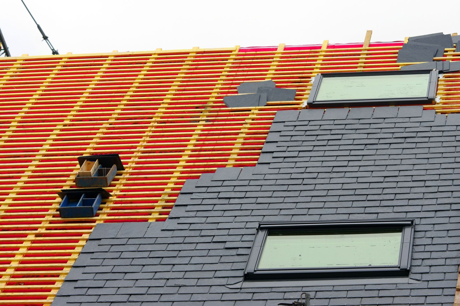 Un toit en construction ; des bardeaux d'ardoise noire recouvrent un côté, des supports en bois.