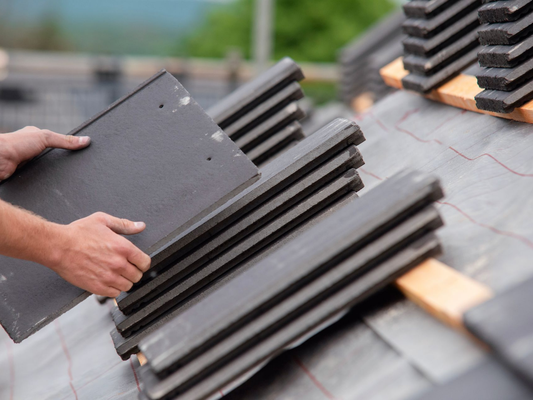 Personne plaçant des tuiles foncées sur un toit pendant la construction.