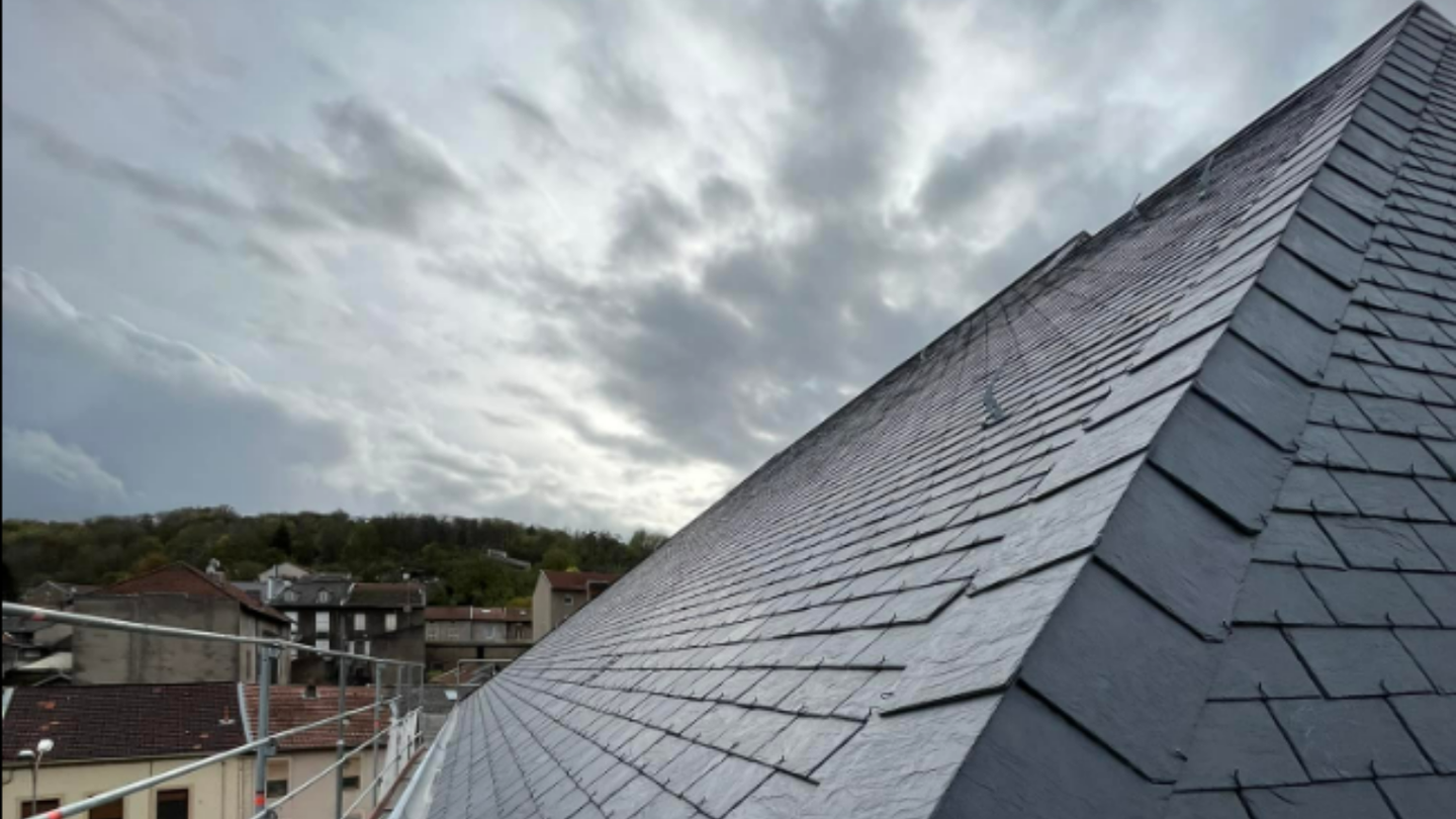 Toit en ardoise d'un bâtiment contre un ciel nuageux dans un décor urbain.