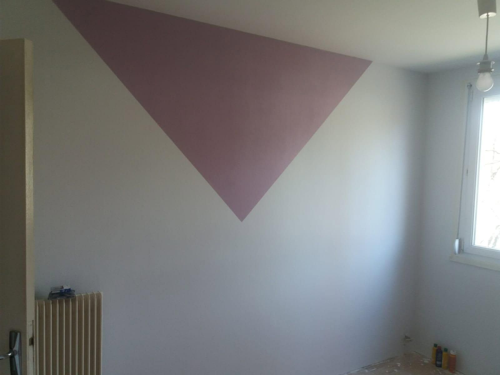 Pièce vide avec un grand triangle rose peint sur un mur blanc près d’une fenêtre.