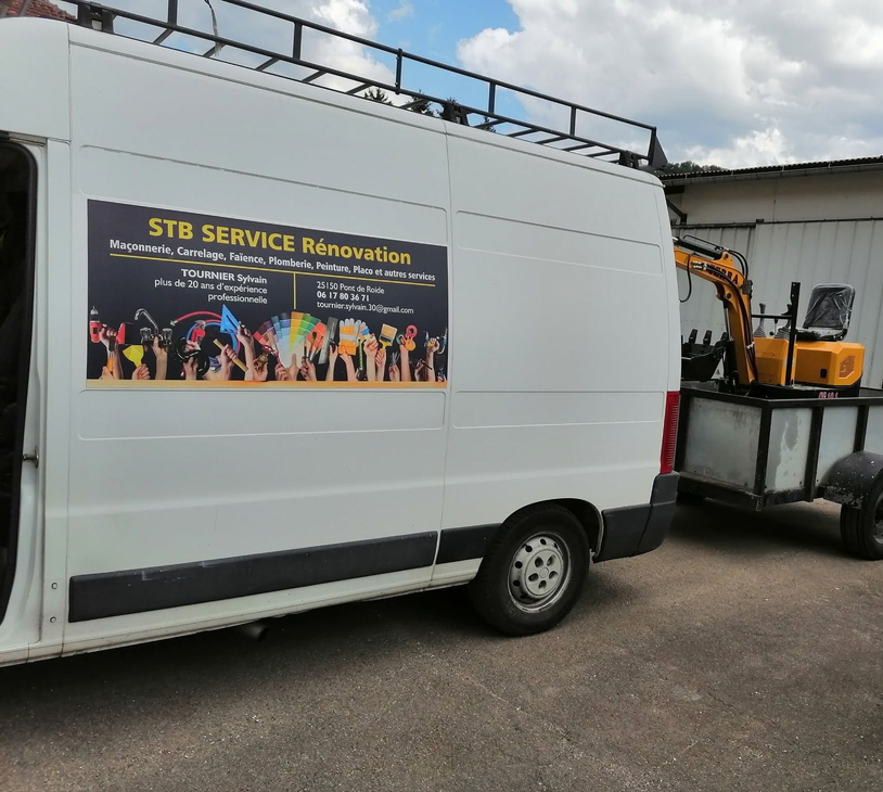 Fourgon de service blanc avec une enseigne STB Services Rénovation, garé à côté d’engins de chantier en extérieur.