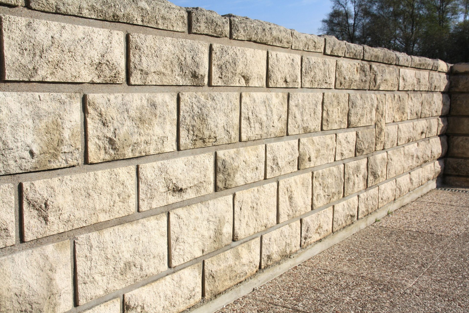 Mur de soutènement en pierre le long d’un chemin de gravier, en plein jour.