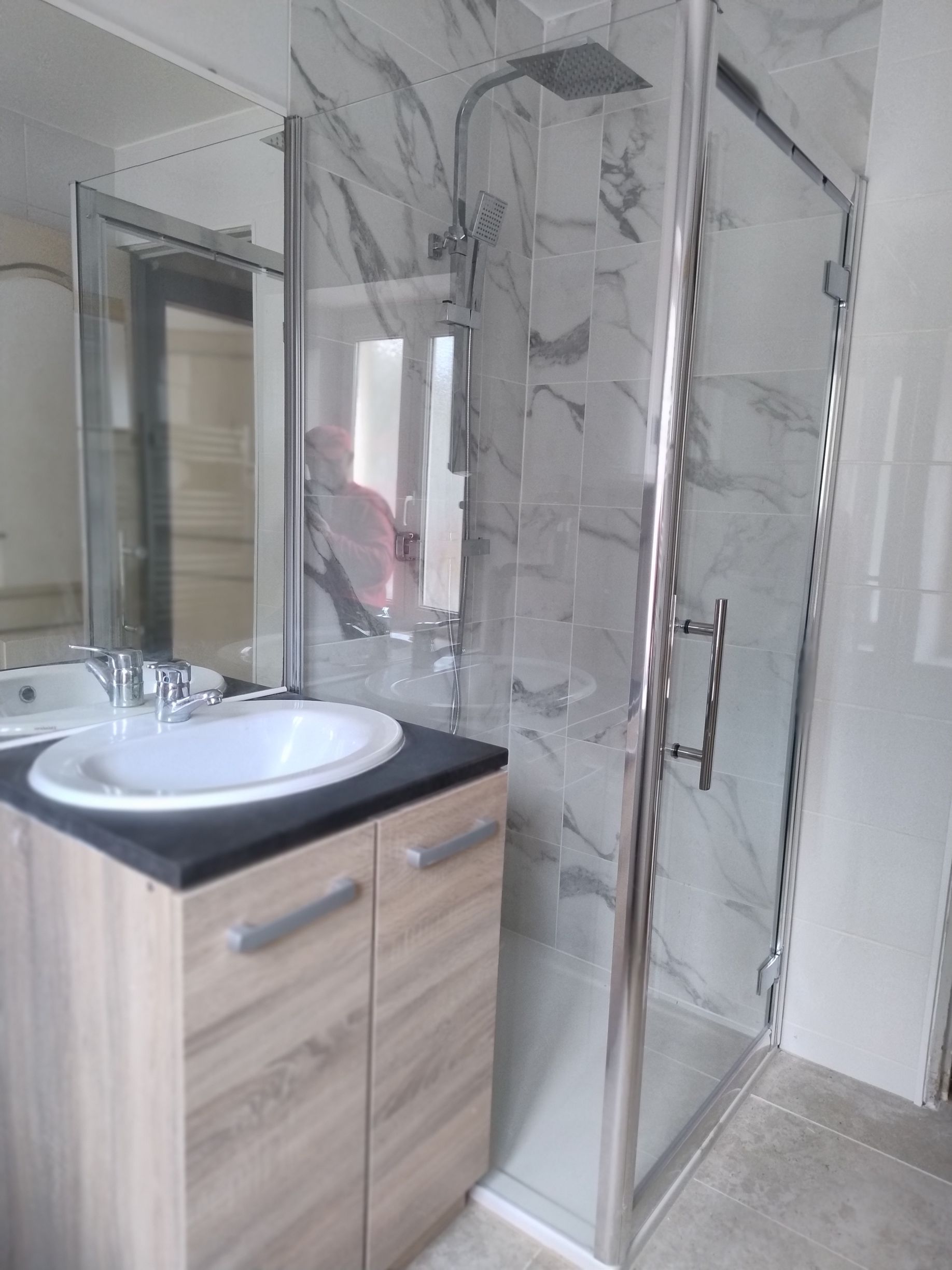 Salle de bains moderne avec meuble sous-vasque en bois, vasque ronde et cabine de douche en verre avec murs effet marbre.