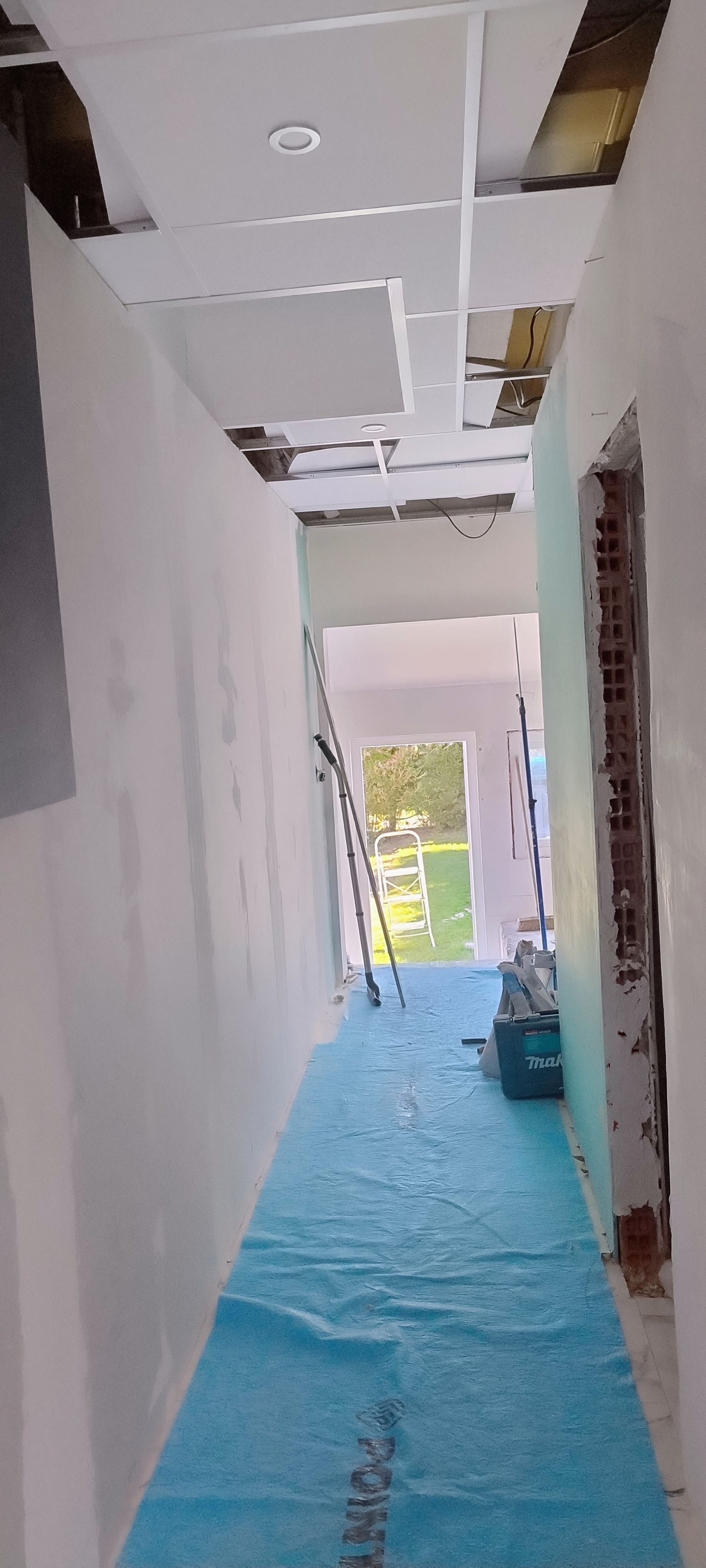 Couloir étroit en cours de rénovation, avec une protection bleue au sol et des panneaux de plafond.