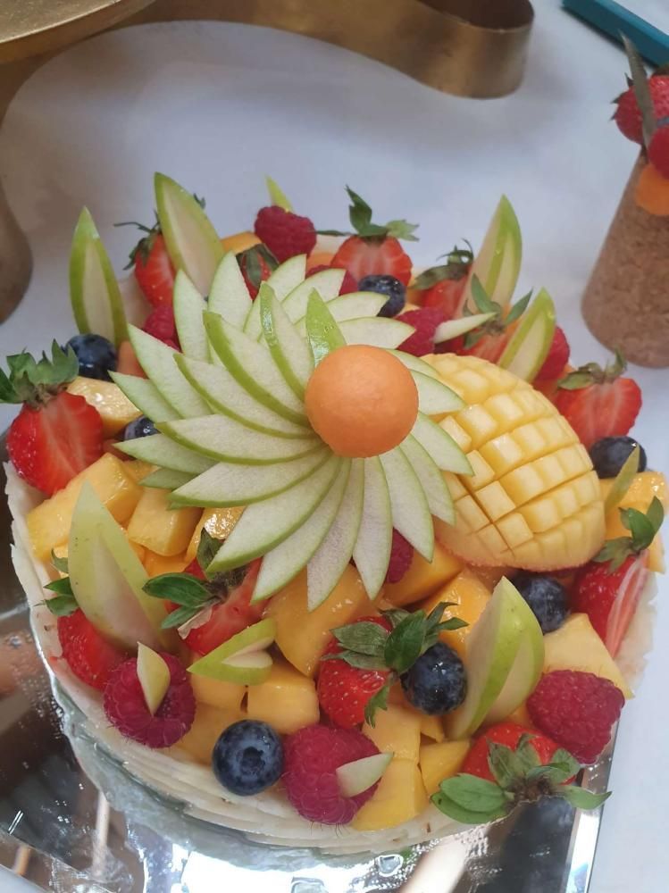 Plateau de fruits avec des fraises, du melon, du kiwi, de l’ananas et une orange au centre, sur un plateau