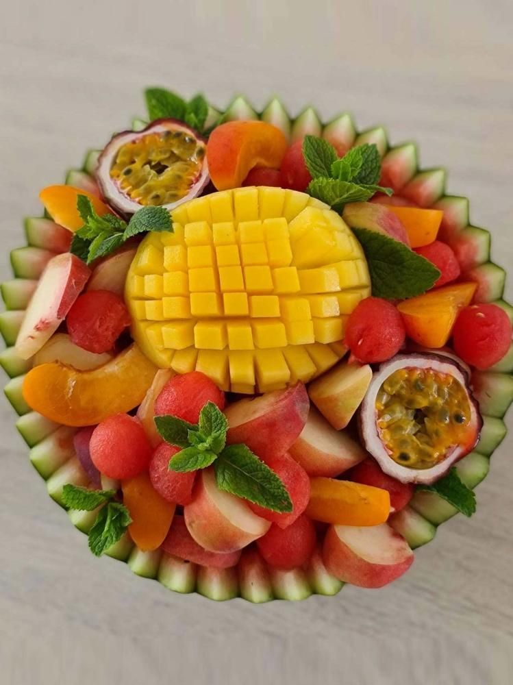Plateau de fruits colorés avec de la mangue, des fraises, de la pastèque, du kiwi et des fruits de la passion autour d’une mangue coupée en tranches au centre