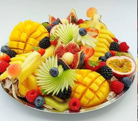 Assiette de fruits colorés avec de la mangue, de l’ananas, des fruits rouges, du kiwi et des tranches de fruit de la passion, sur une assiette blanche