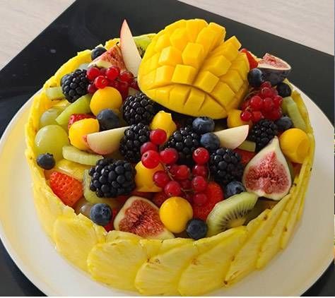 Gâteau jaune glacé garni de fruits, avec de la mangue, des baies, du kiwi, des figues et des tranches de poire, sur une assiette blanche