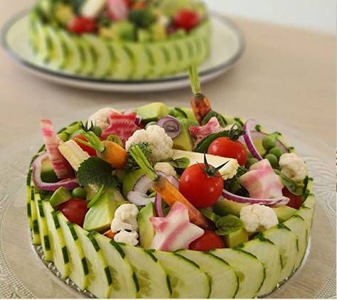Salade de légumes colorée dans un bol sculpté dans un concombre, avec des tomates cerises, du chou-fleur et des oignons