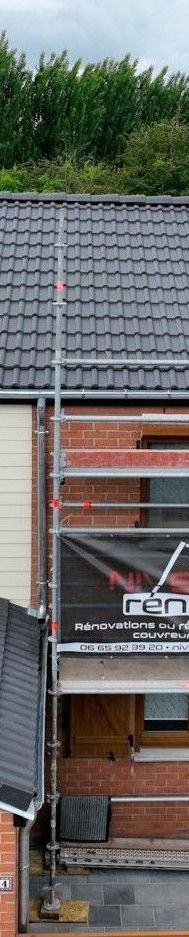 Bâtiment en briques avec toit de tuiles orange, porte grise et ciel bleu.